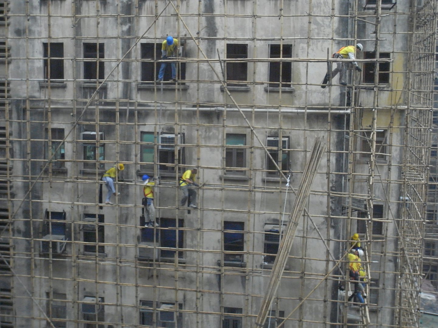 Operai edili salgono su un ponteggio di bambù sulla facciata di un edificio.